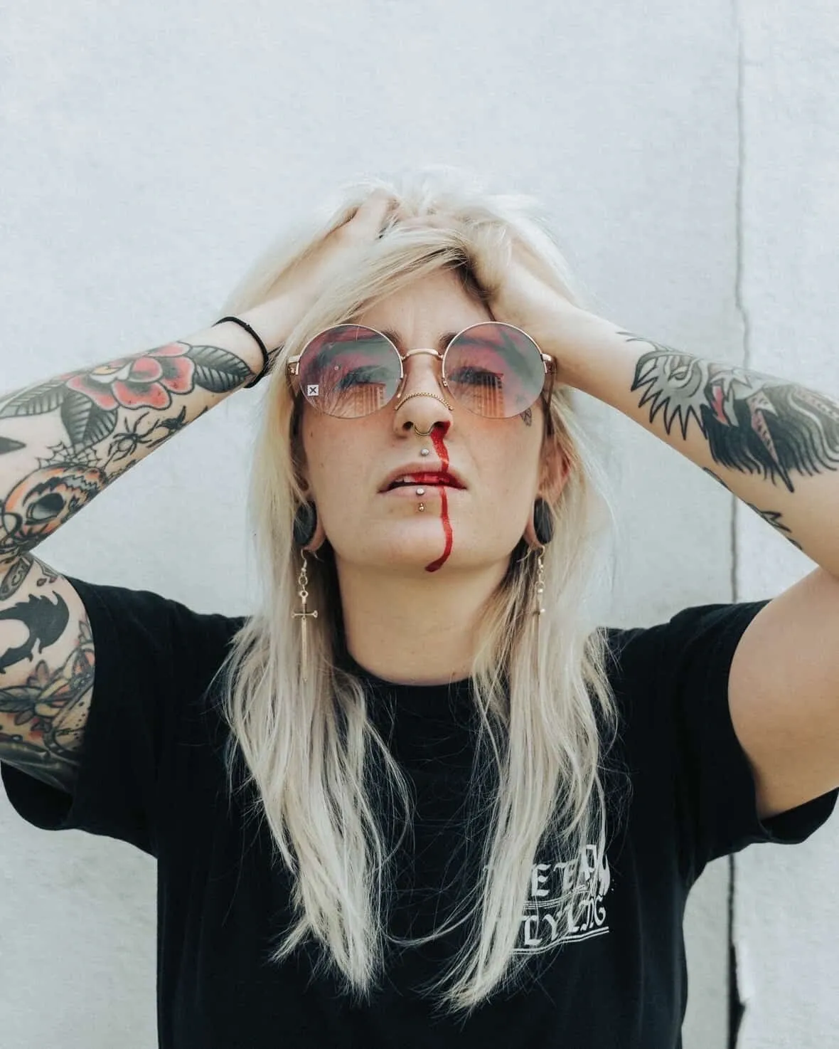 Person with nosebleed and tattoos, wearing sunglasses.