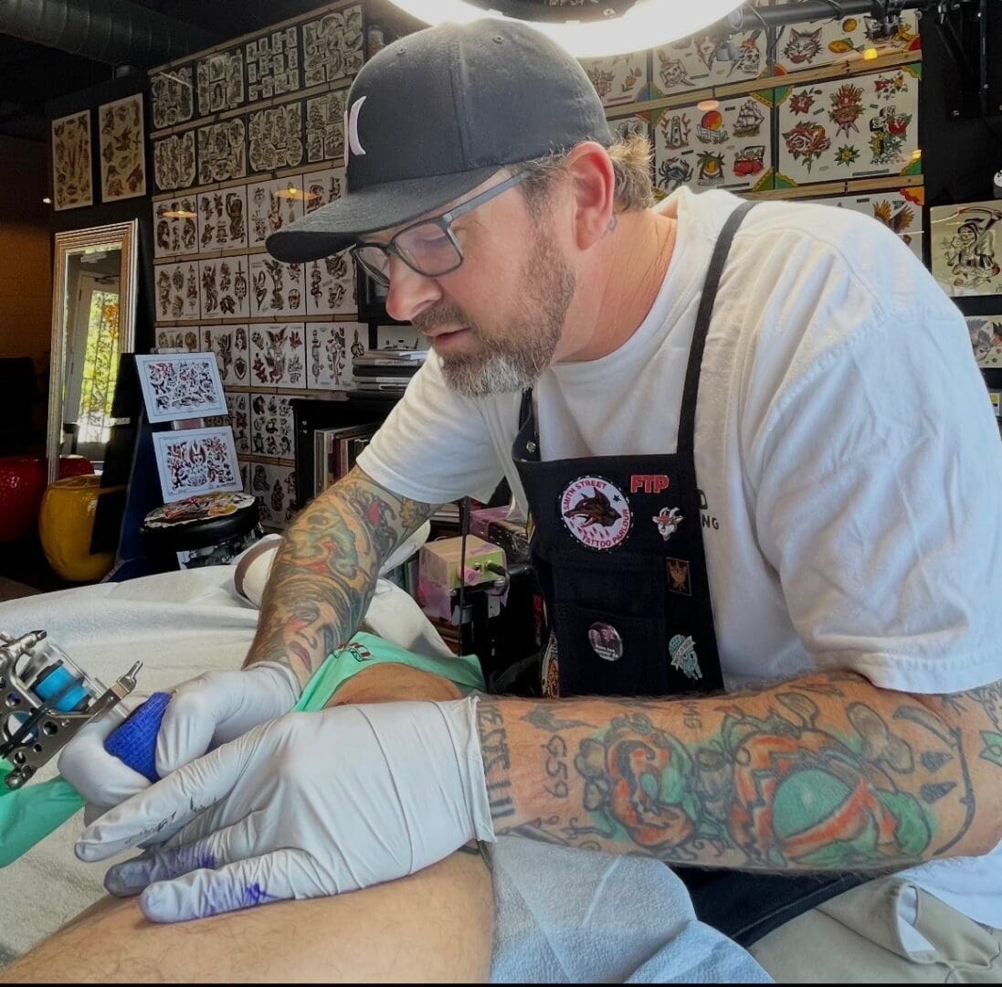 Tattoo artist working on a client's leg.