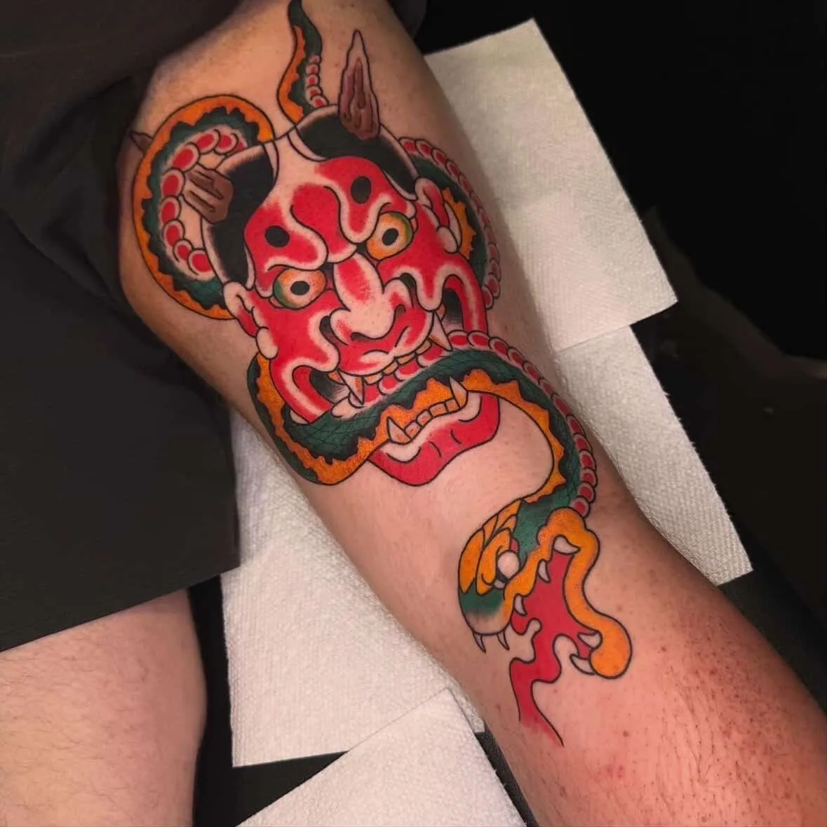 Tattoo of colorful demon mask on leg.